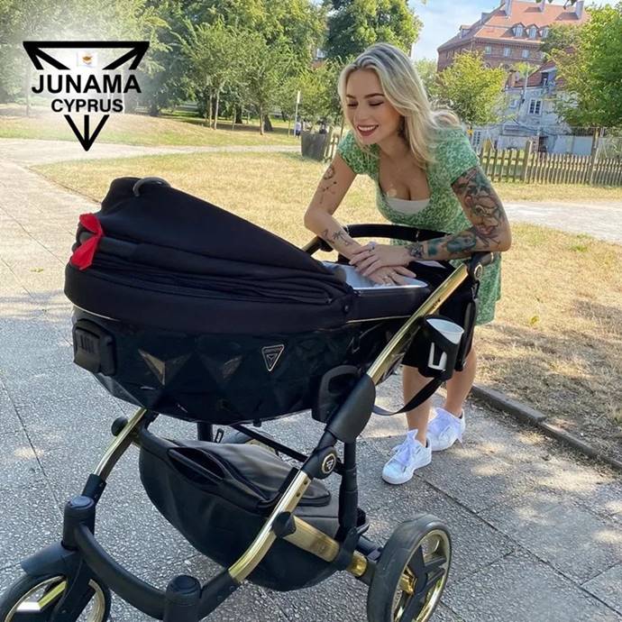 Czy czarny wózek się nagrzewa – kobieta pochyla się nad czarną gondolą w letni dzień w cieniu.